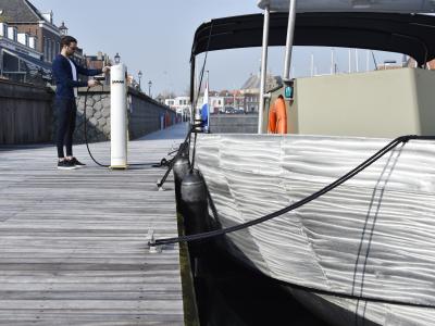 Boot aan steiger, persoon sluit kabel aan op laadpaal
