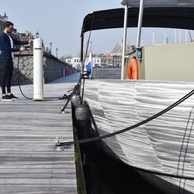 Boot aan steiger, persoon sluit kabel aan op laadpaal